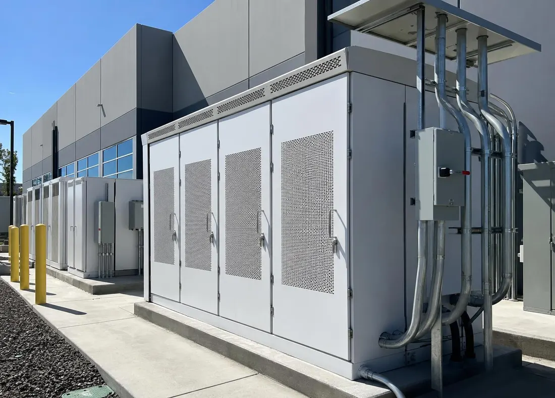 Commercial battery energy storage cabinets on a concrete pad beside a warehouse