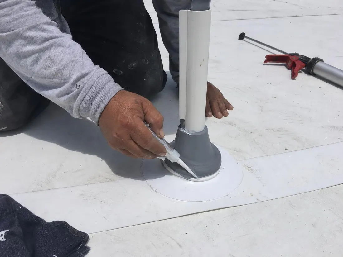 Roofer sealing a pipe boot penetration on a white single-ply commercial roof